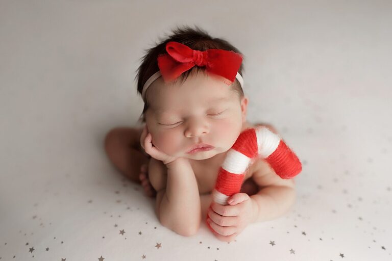 newborn girl in red bow holding candy cane prop